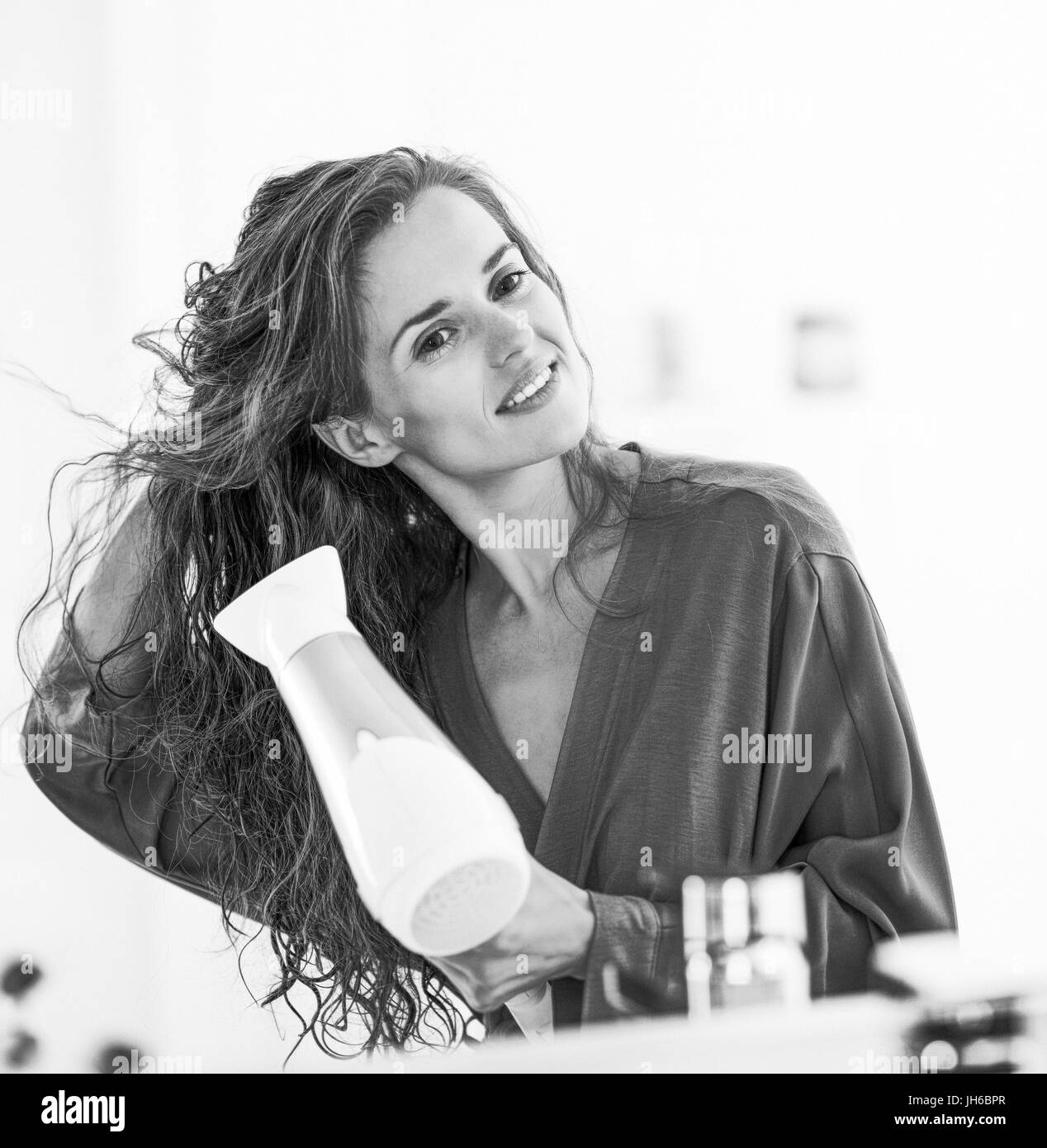Happy young woman blow drying hair in bathroom Stock Photo - Alamy