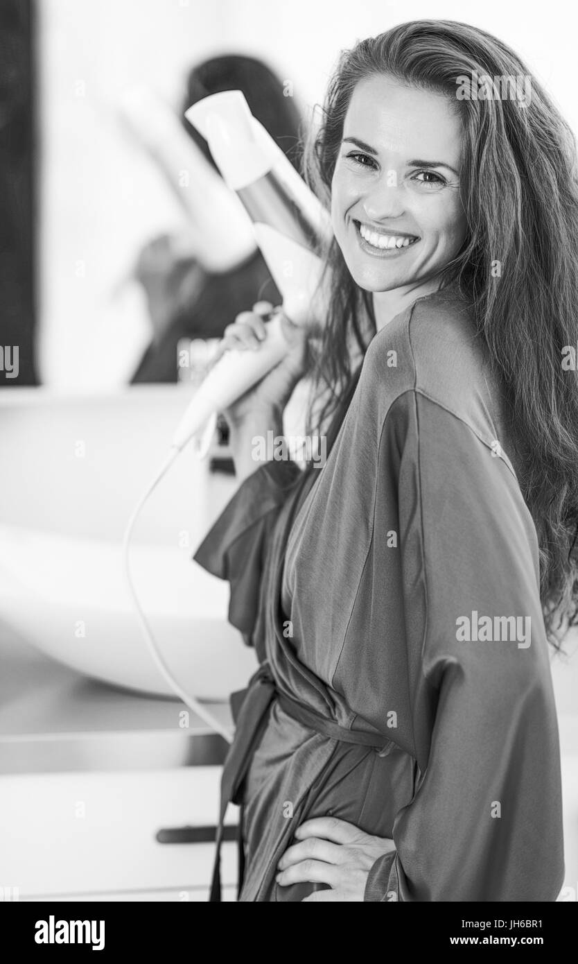 Portrait of smiling young woman with blow dryer in bathroom Stock Photo