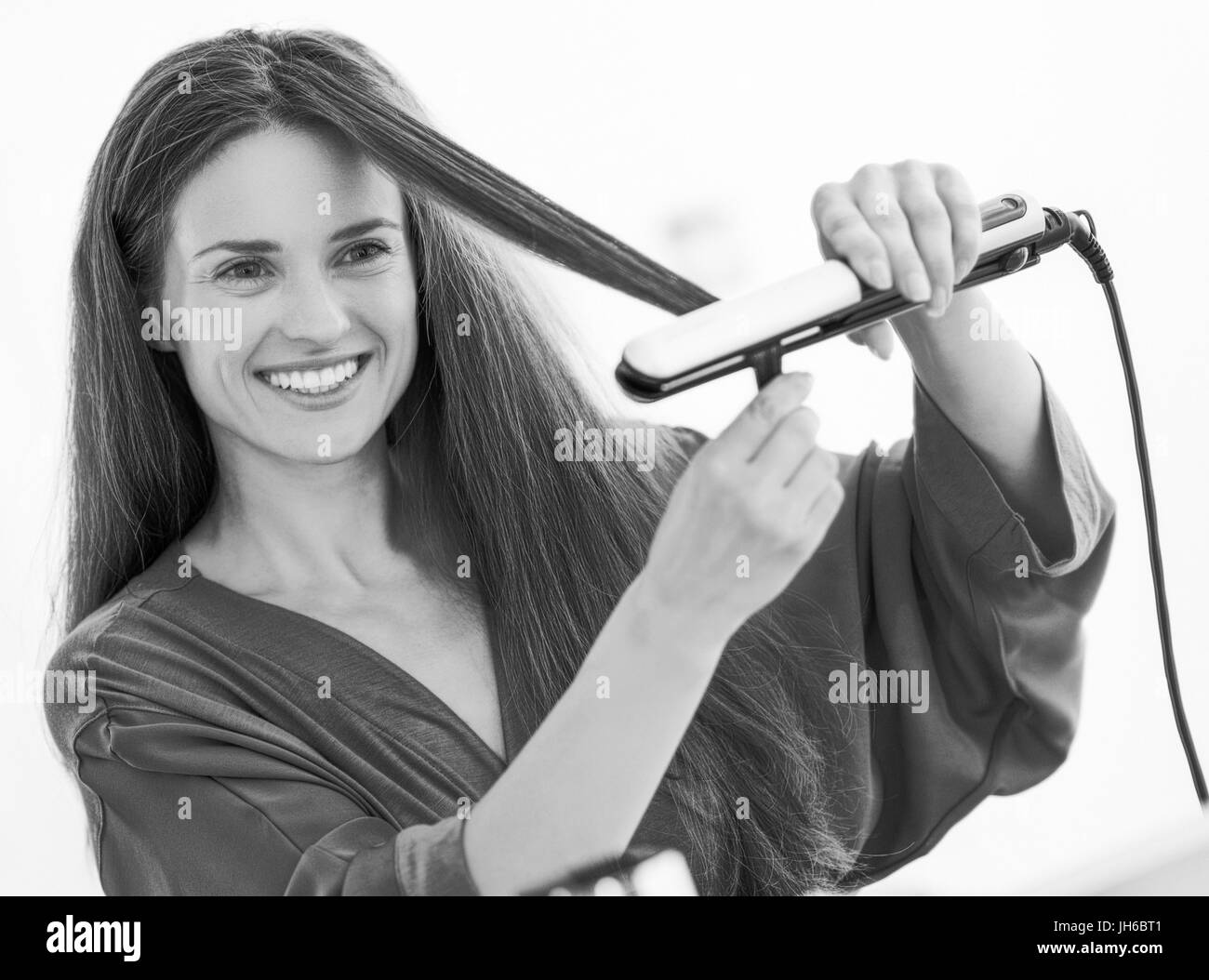 Happy young woman straightening hair with straightener Stock Photo