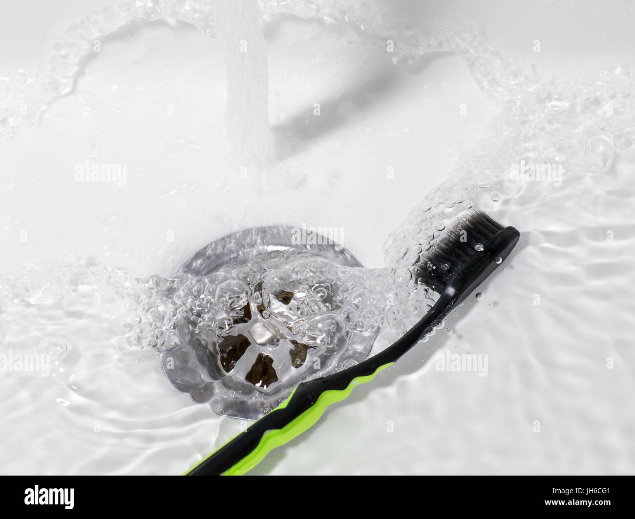 Toothbrush lying in the sink with running water. Bathroom theme Stock Photo