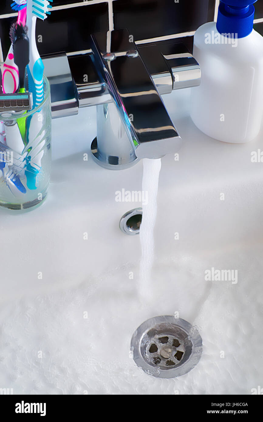 Modern water tap, water in the sink and  hygiene objects. Bathroom scene Stock Photo