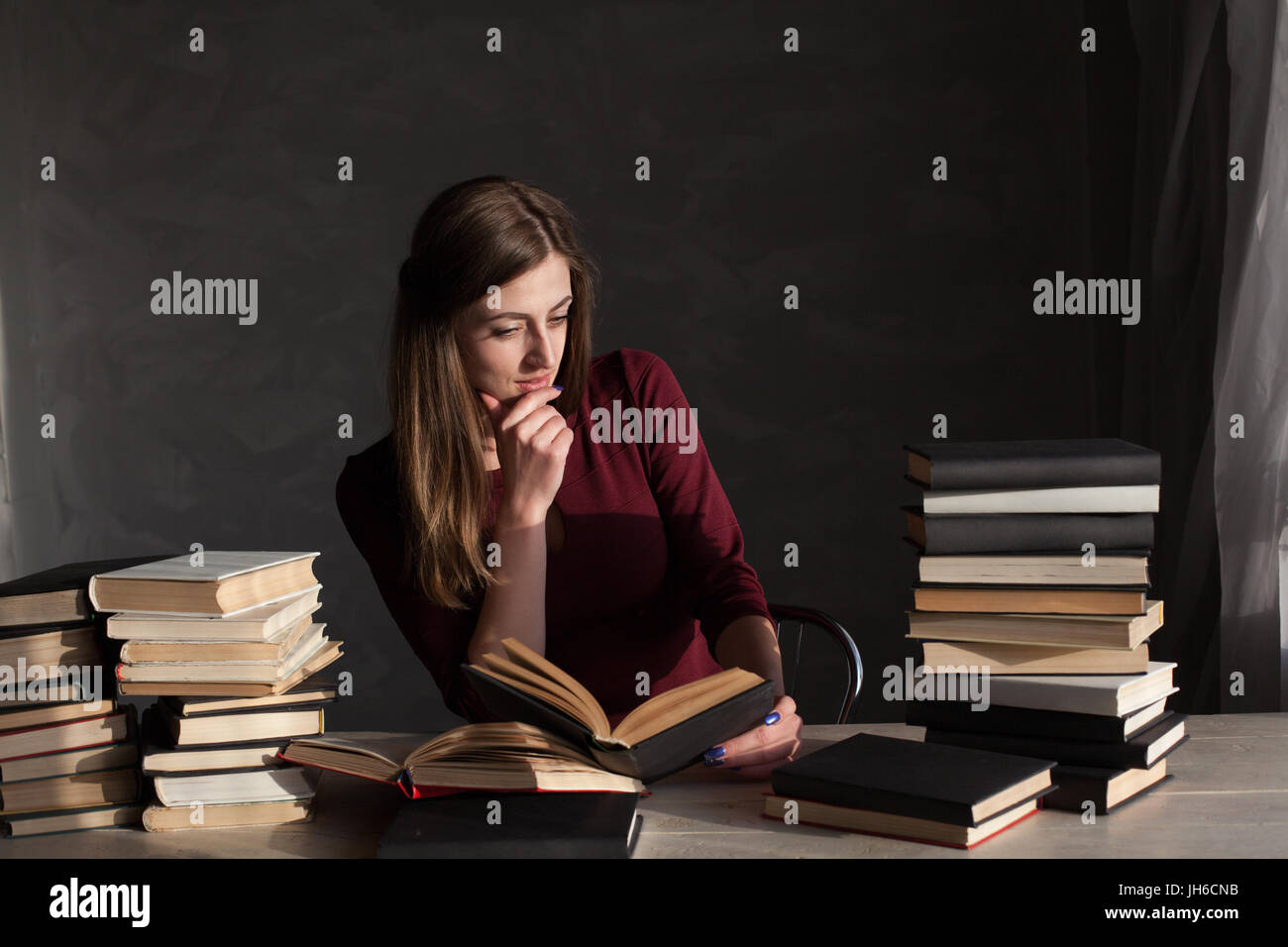 the girl sitting at the table reading a lot of books Stock Photo