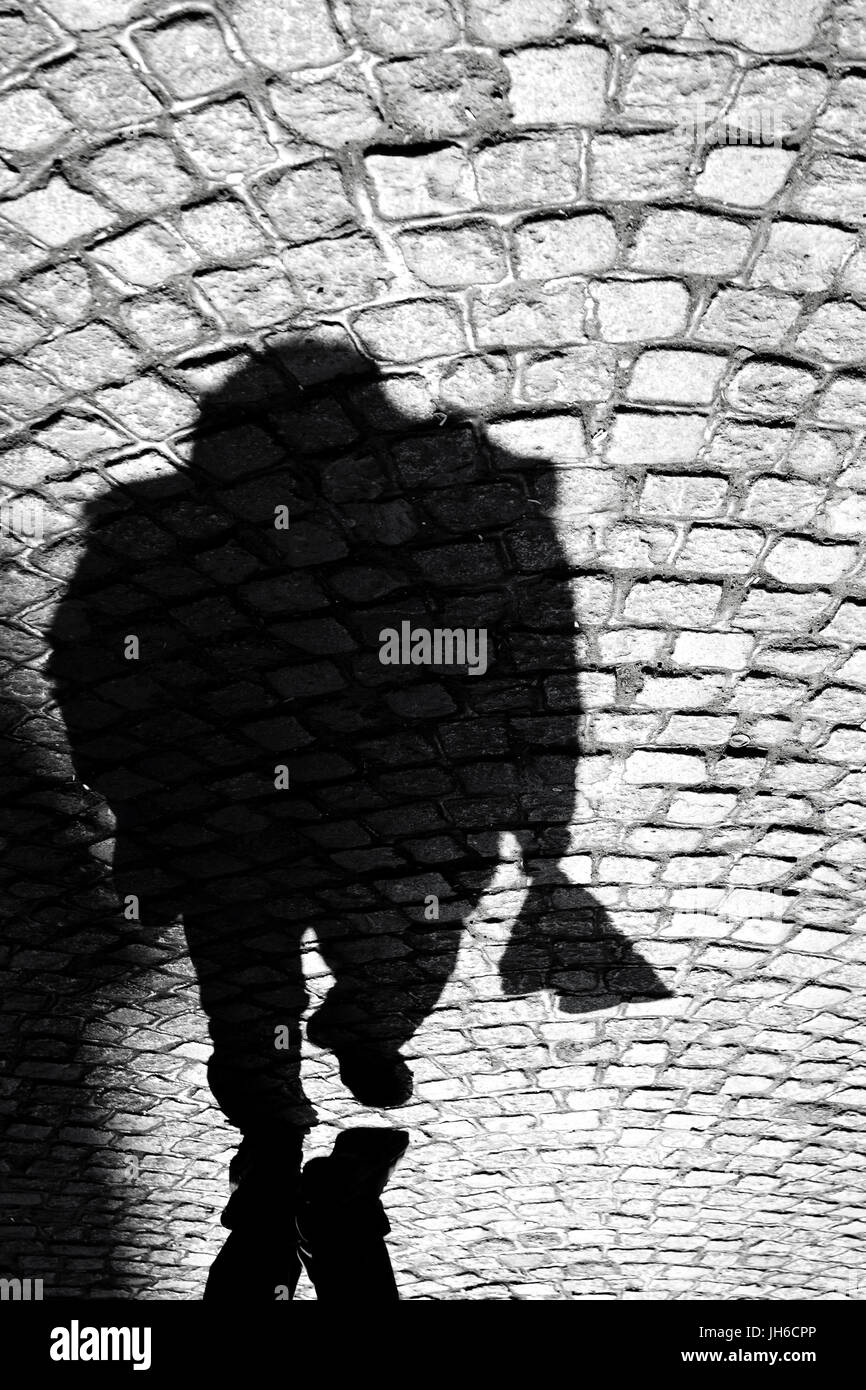 Blurry shadow silhouette of a man on the old cobbled road in Balkans in black and white; Stock Photo