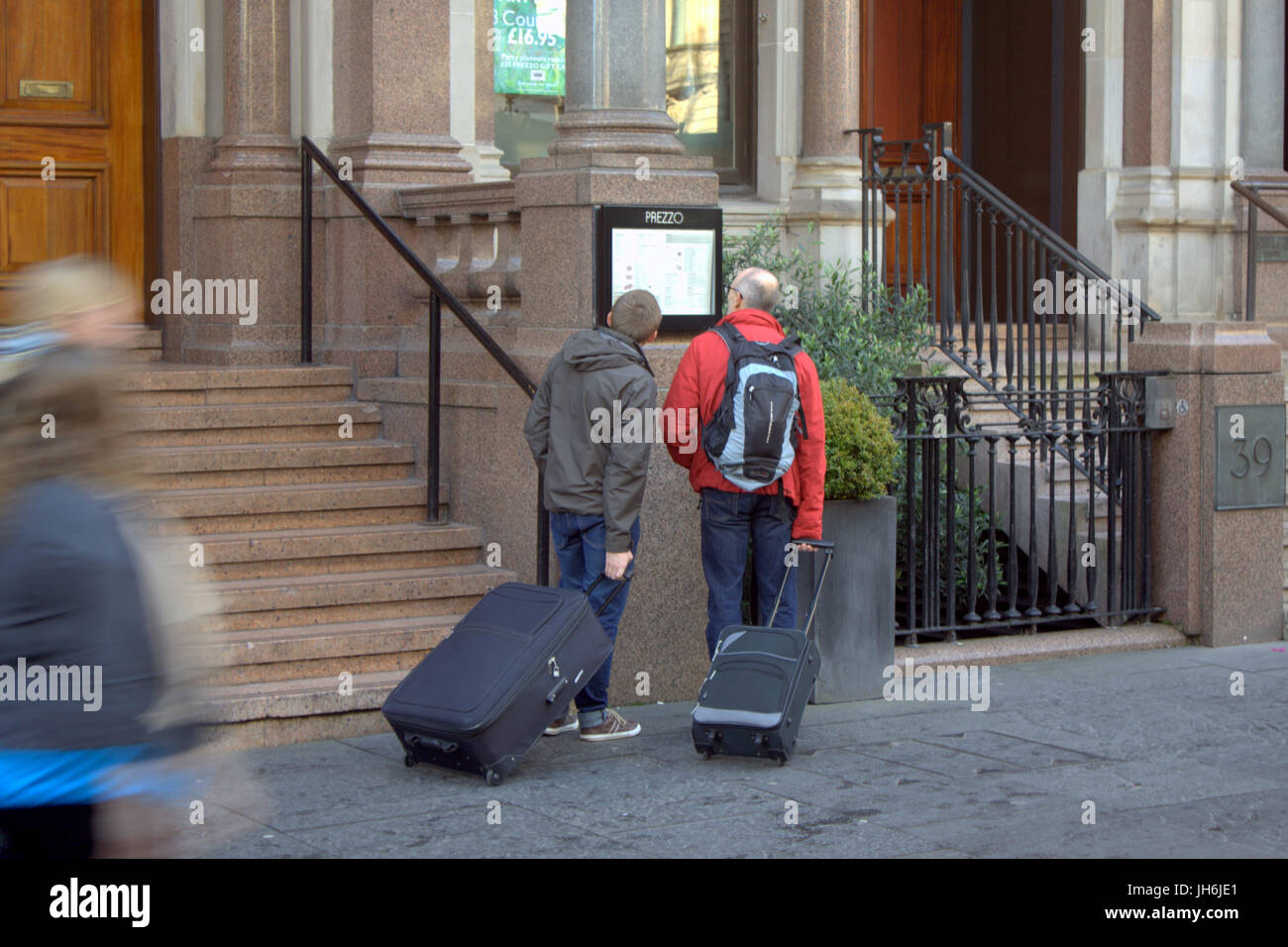 Tourists with baggage read the price list for local restaurant near George Square in Glasgow city centre Stock Photo