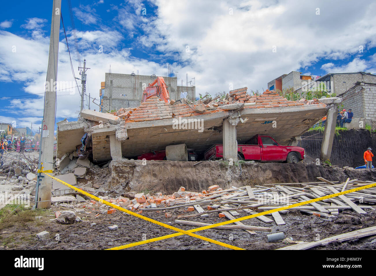 Quito, Ecuador - April,17, 2016: House destroyed by Earthquake, with a red car caught under the destroyed construction, and heavy machinery cleaning t Stock Photo