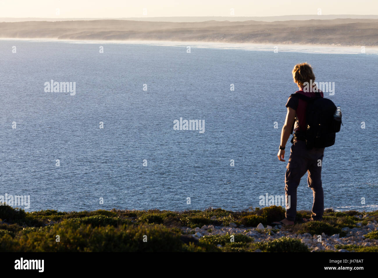 A hiker stops to look at a distant view of a beautiful coastline from a high view point above the sea in southern Australia. Stock Photo