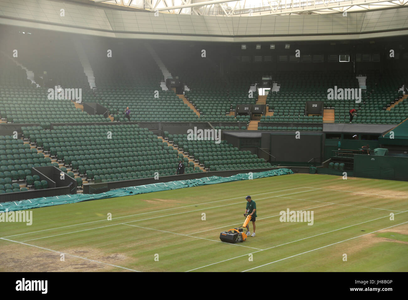 Ground staff cut the grass on centre court prior to the start of the action on day ten of the Wimbledon Championships at The All England Lawn Tennis and Croquet Club, Wimbledon. Stock Photo