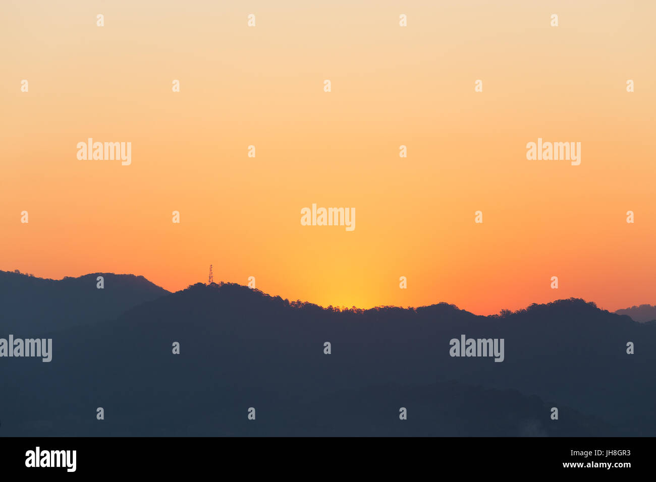 A mountain range and telegraph tower is silhouetted by a beautiful golden glowing sunset in Australia. Stock Photo