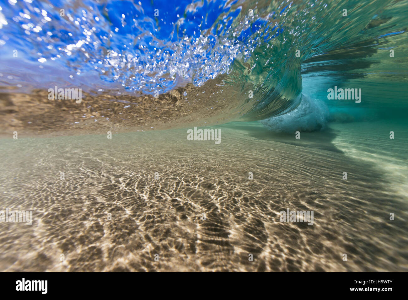 An underwater shot of beneath a wave breaking in crystal clear water over a sand bottom. Stock Photo