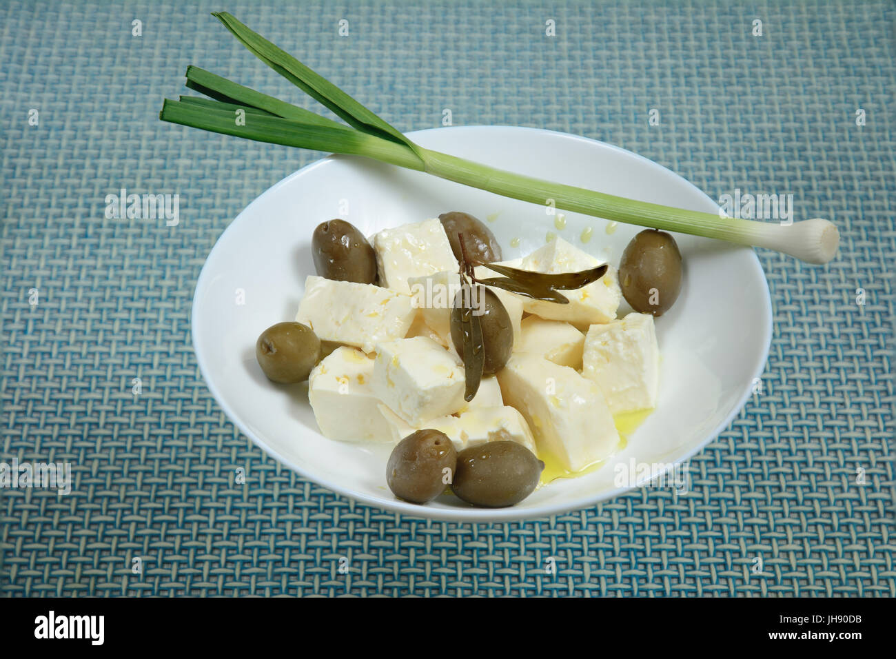 Pieces of white brine cheese and olives were poured over with extra virgin olive oil. Green garlic is lying on the edge of a bowl. Stock Photo
