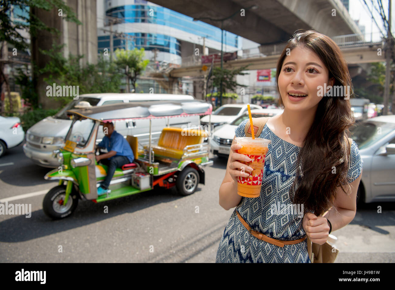 Lifestyle hipster asian woman drinking healthy traditional thai milk tea walking on downtown street of bangkok, thailand. Happy young asian girl with  Stock Photo