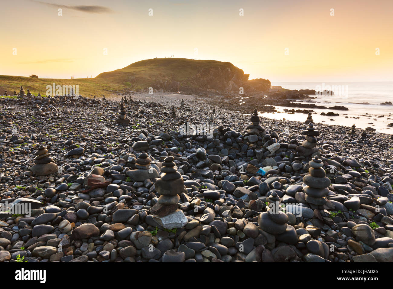 The golden morning light illuminates a beach of pebbles and rock cairns near Port Macquarie, Australia. Stock Photo