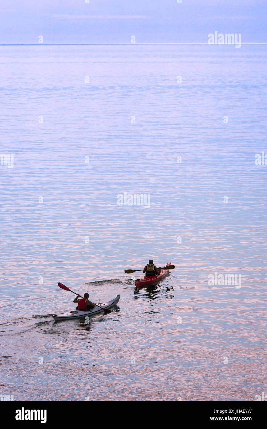 Kayak sea, two kayakers set off at dawn across the bay at Alghero, north-west Sardinia. Stock Photo