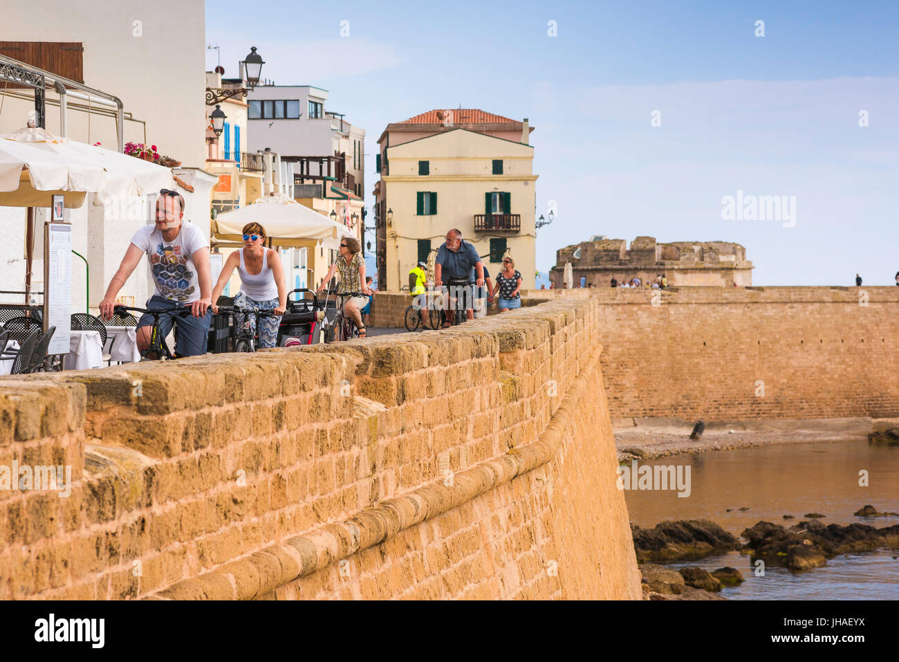 Alghero Sardinia seafront, tourists cycle along the medieval seawall on the west side of Alghero, north-west sardinia. Stock Photo