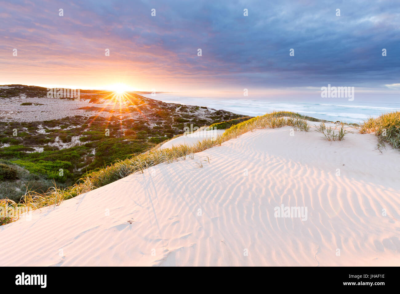 The sun bursts above the horizon, illuminated the sand dunes and surrounding coastline in this beautiful seascape. Stock Photo
