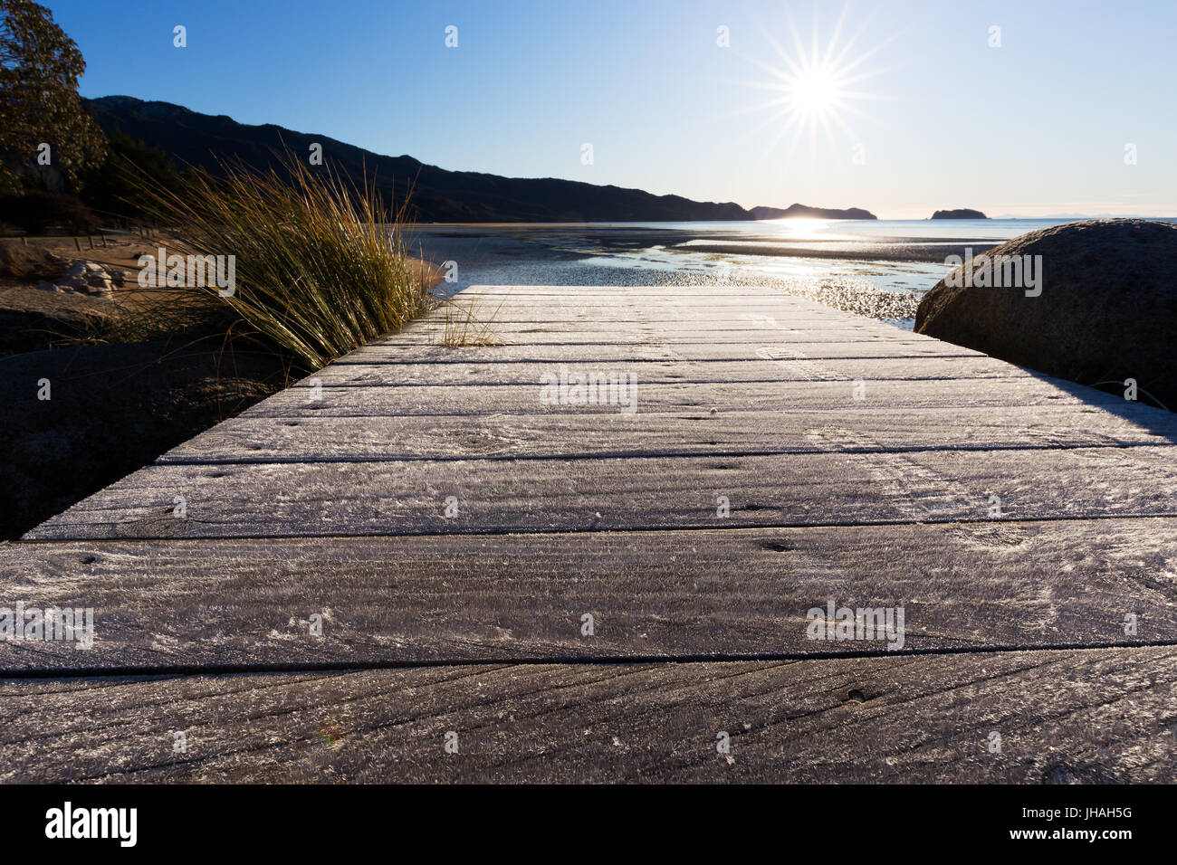 Frosty footprints on a wooden board walk during a crisp sunrise in New Zealand. Stock Photo