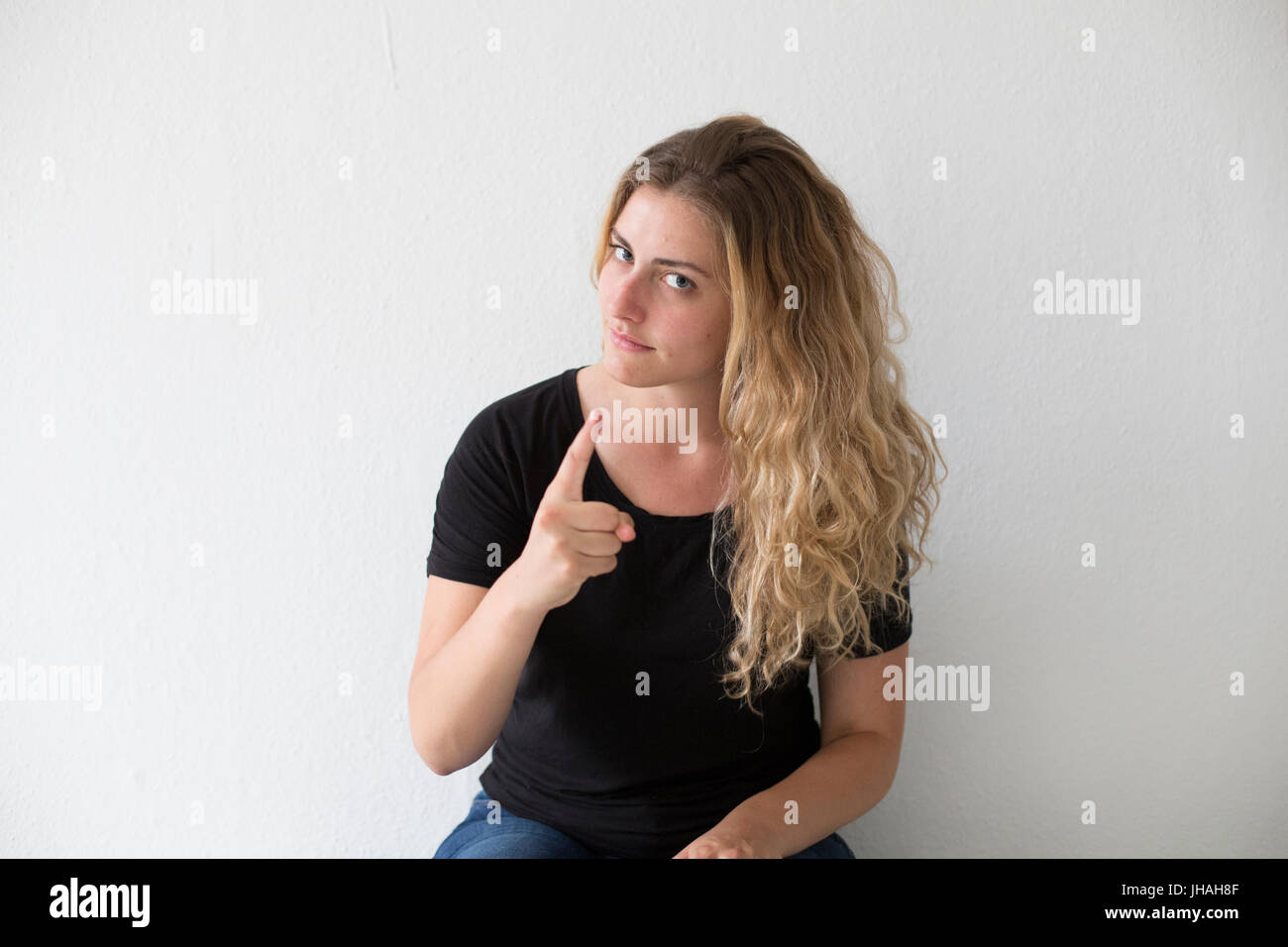 Young, blonde, caucasian woman expresses negative emotion, anger, screaming and finger pointing at viewer and photographer on a white background. Stock Photo