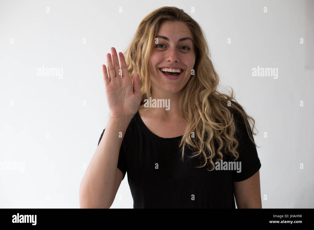 Young, blonde, beautiful, caucasian milennial woman expressing excitement and happiness while waving against a white background. Inviting, welcoming. Stock Photo