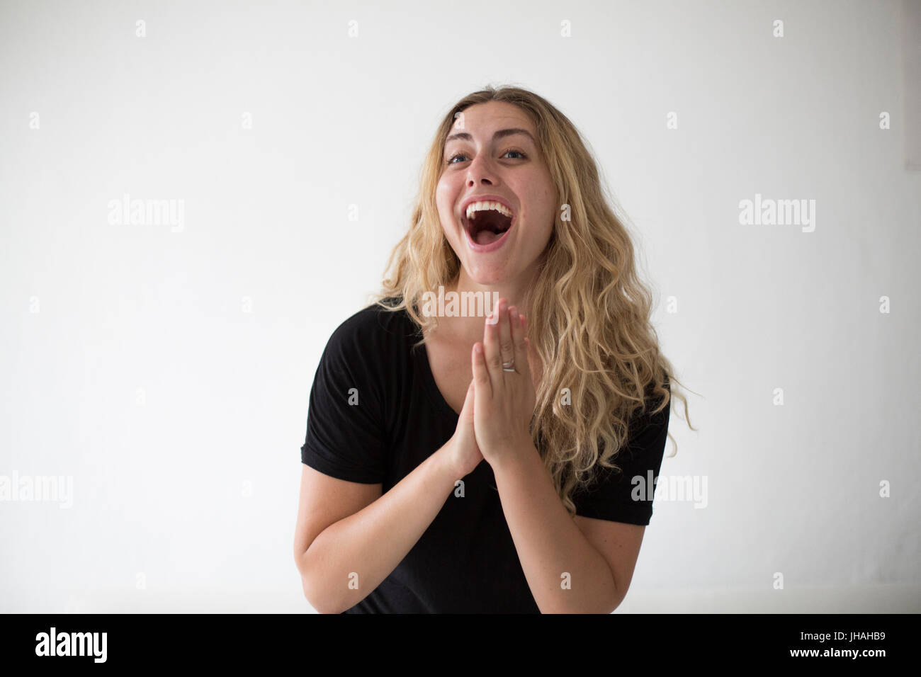 Young, blonde woman cheering and clapping in excitement and happiness against a white background in natural day light. A beautiful millenial. Stock Photo