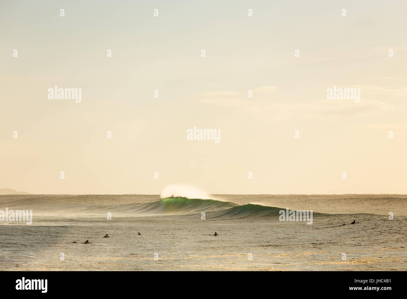Two wave peaks break in golden morning light around surfers at an Australian beach. Stock Photo