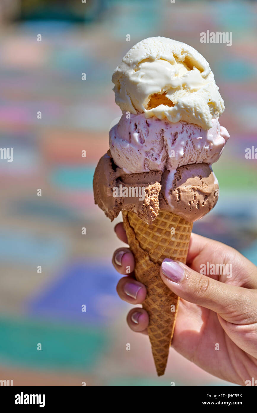 Summertime enjoyment: Female hand holding three scoop ice cream waffle cone Stock Photo