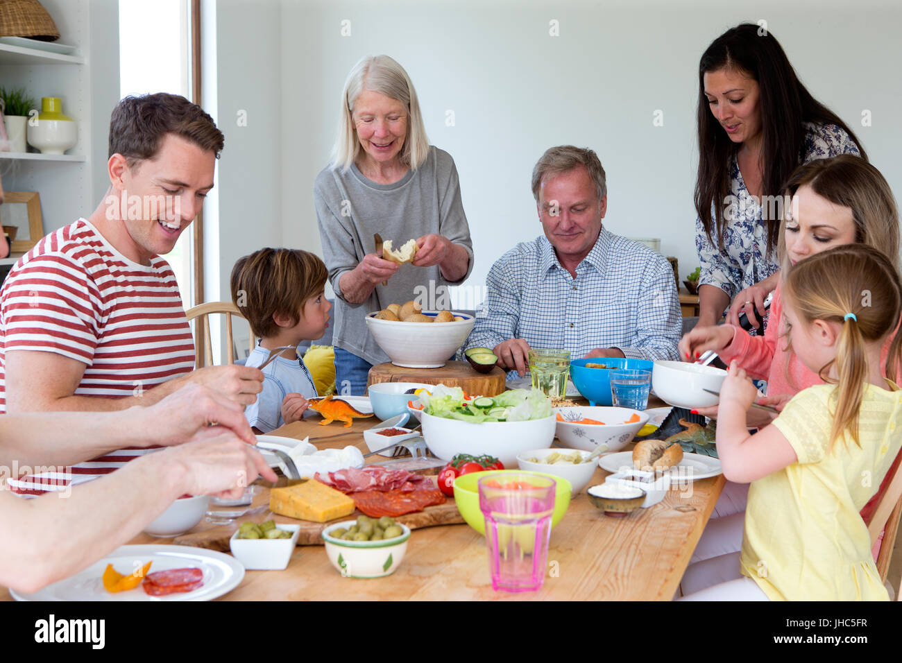 Large family are sat round a table in the dining room of a home. They are eating mediterranean style food. Stock Photo