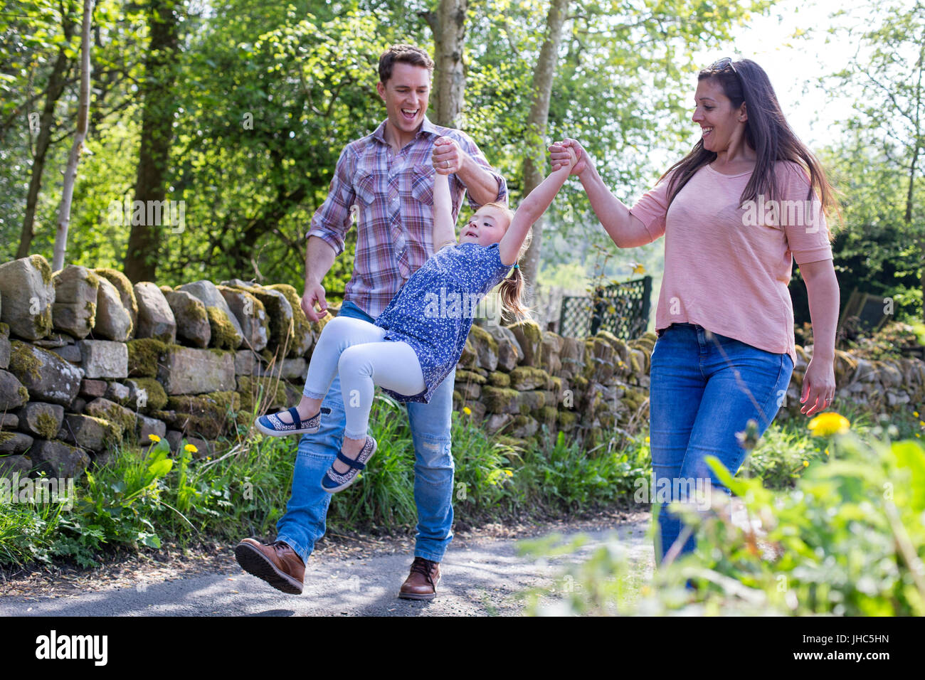 Little girl being swung by her parents as they walk down a country footpath. Stock Photo