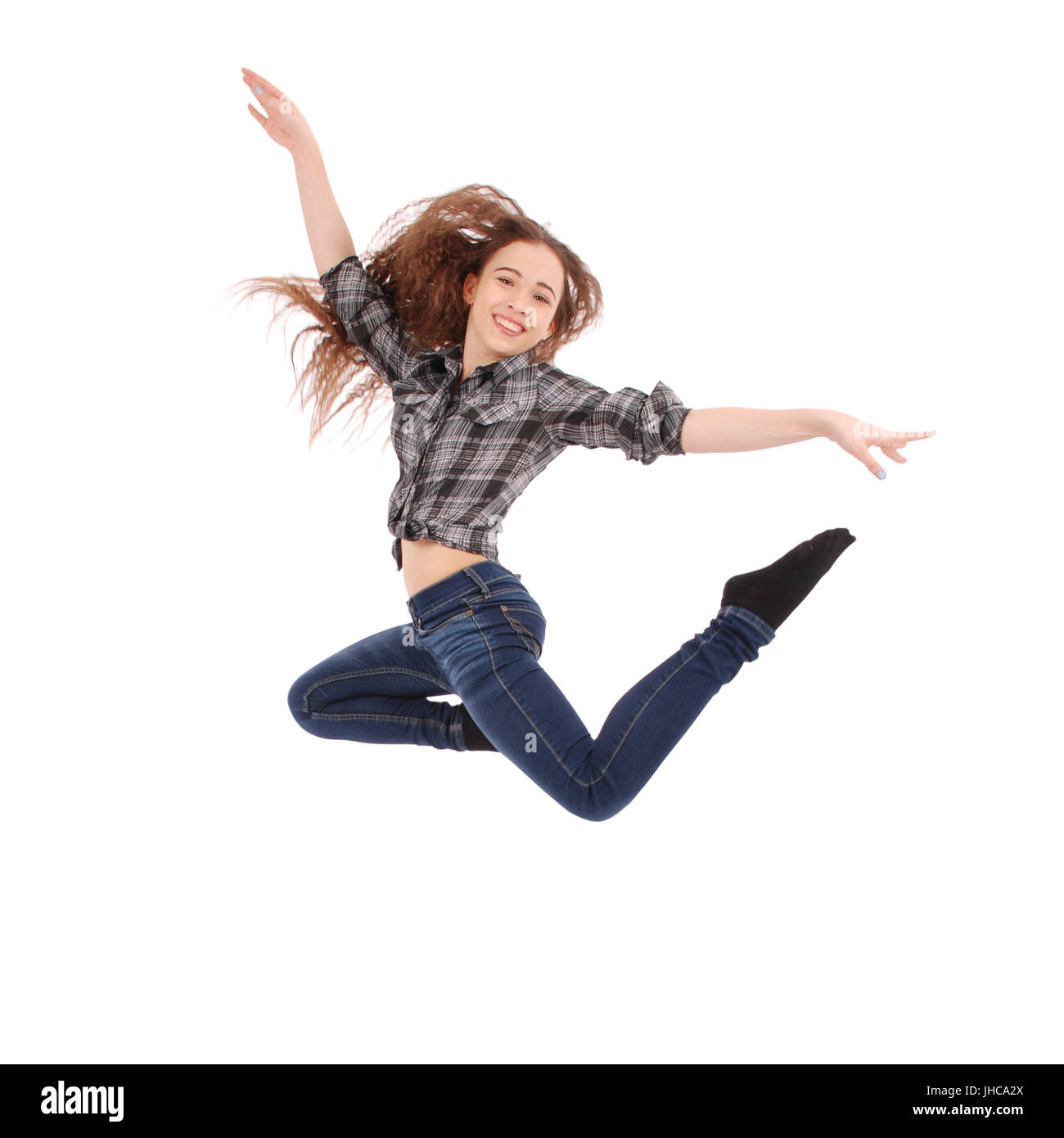 Pretty cute caucasian girl wearing a checkered shirt and blue jeans. The girl is jumping and smiling. Stock Photo