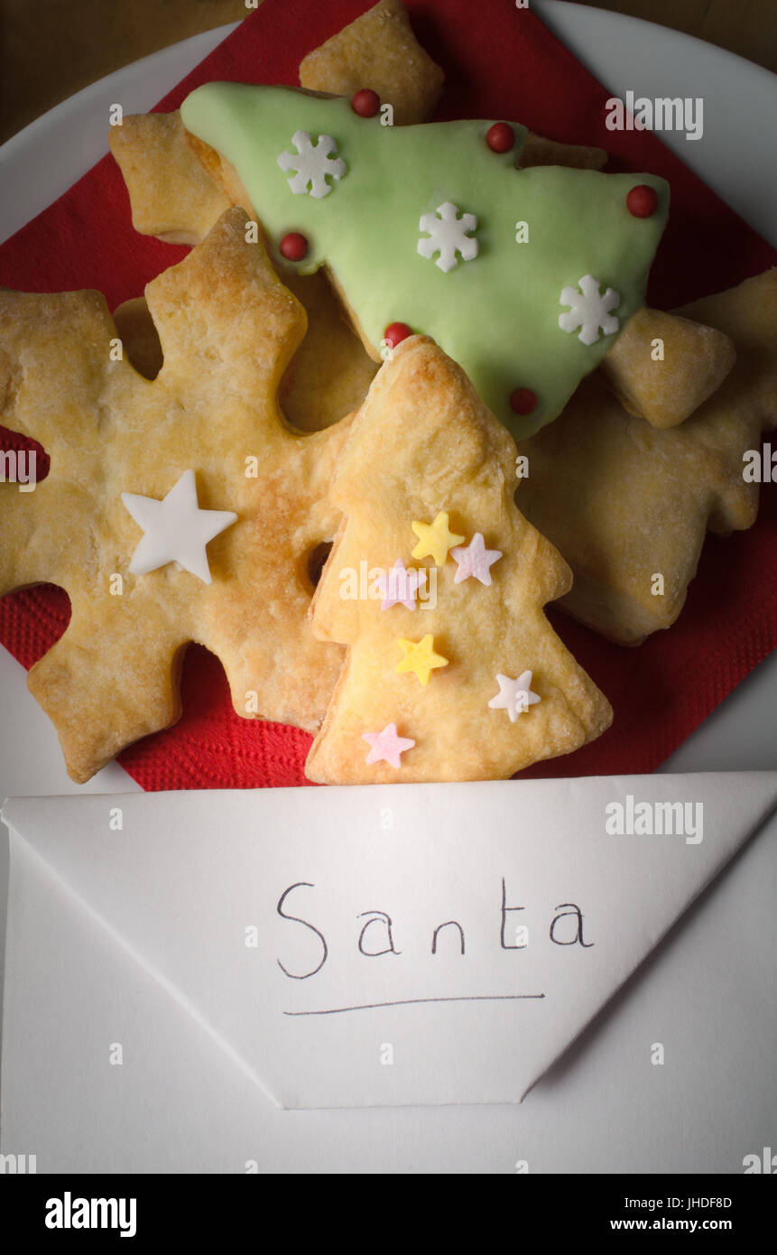 Christmas concept.  Overhead of a plate of shaped Christmas biscuits (cookies)  with an envelope addressed to Santa.  Lit with appearance of torch lig Stock Photo