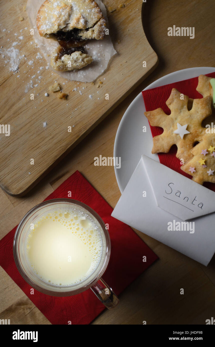 Overhead shot of a Christmas night scene.  A plate of decorated biscuits (cookies), partly eaten mince pie  and glass of milk with envelope addressed  Stock Photo