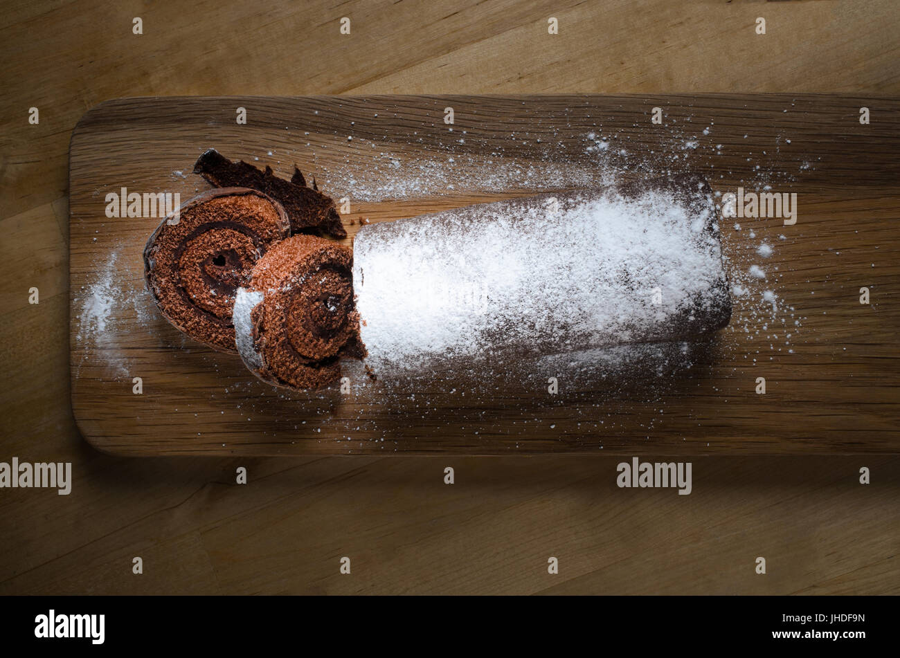 Overhead shot of a full length chocolate Christmas Yule Log or Swiss Roll cake, on long wooden paddle board, dusted with white icing sugar. Stock Photo