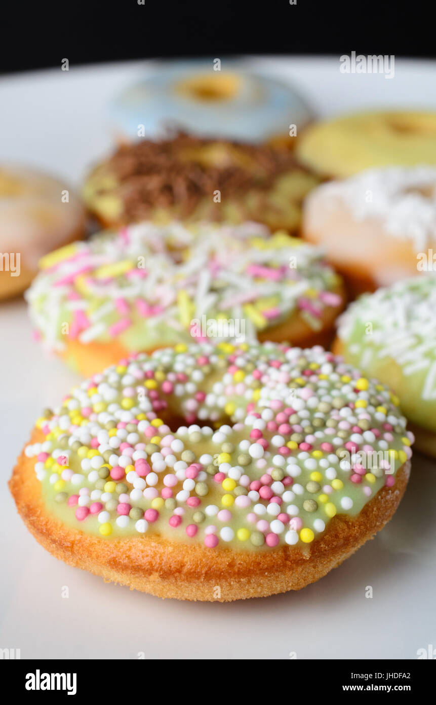 A selection of mini doughnut shaped cakes on a white plate with a variety of decorative sprinkles. Stock Photo