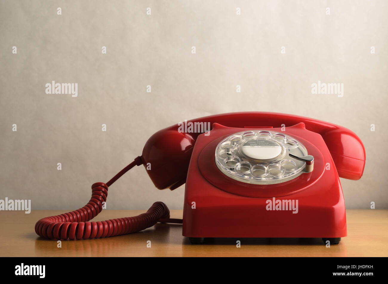 Eye level shot of a retro red telephone (British circa 1960s to 1970s) on a light wood veneer desk or table with off white background providing copy s Stock Photo