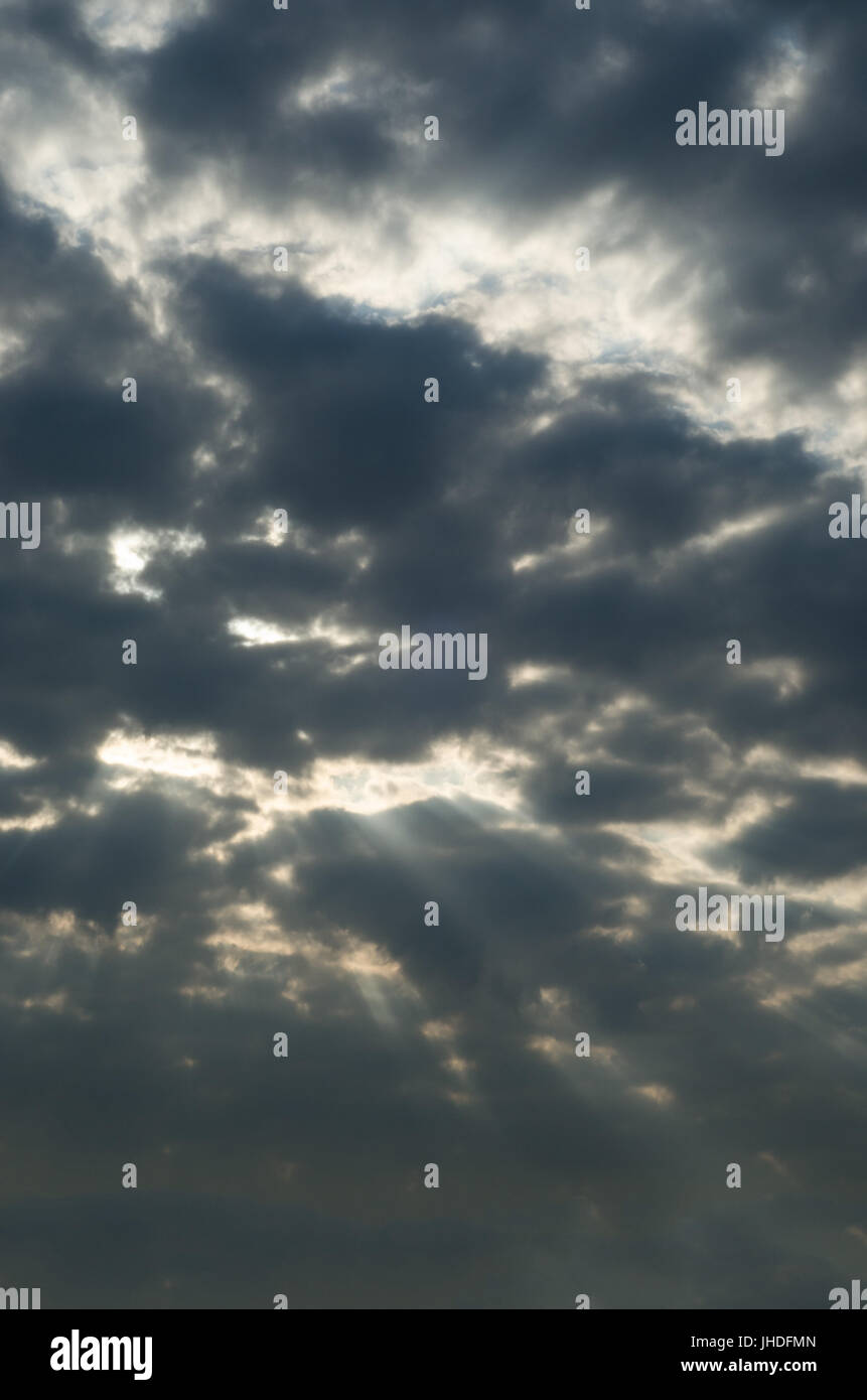 Threatening, ominous dark grey sky with a few rays of bright white sunlight peeping through a gap in the clouds. Stock Photo