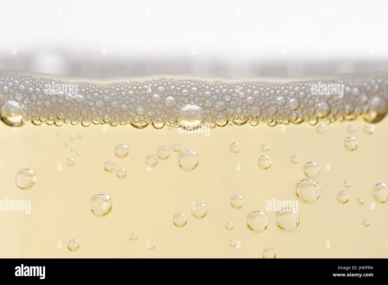 Close up (macro) of  champagne glass, filled with sparkling white wine.  Rising bubbles topped by layer of froth. Eye level shot. Stock Photo