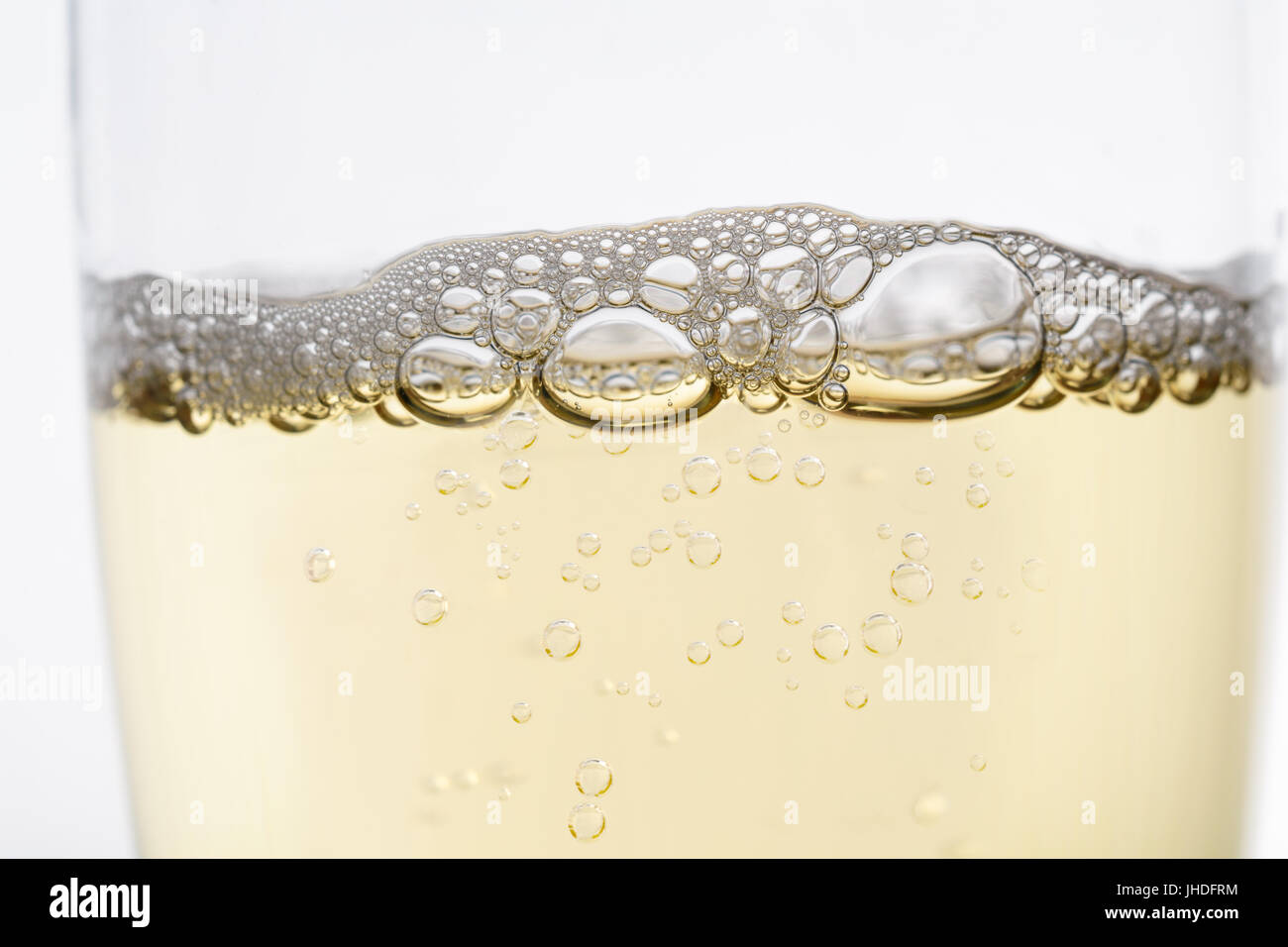 Close up (macro) of sparkling champagne flute style glass, wiith rising bubbles topped by layer of froth. Stock Photo