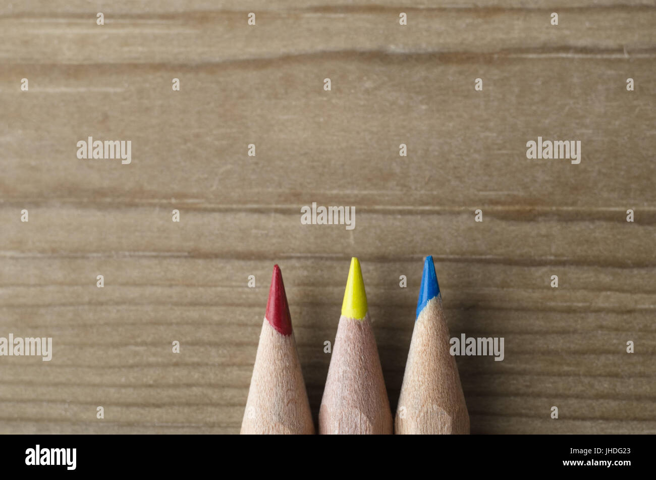 Three pencils lined in a row and pointing upwards towards wooden copy space, representing the primary colours model of red, yellow and blue. Stock Photo