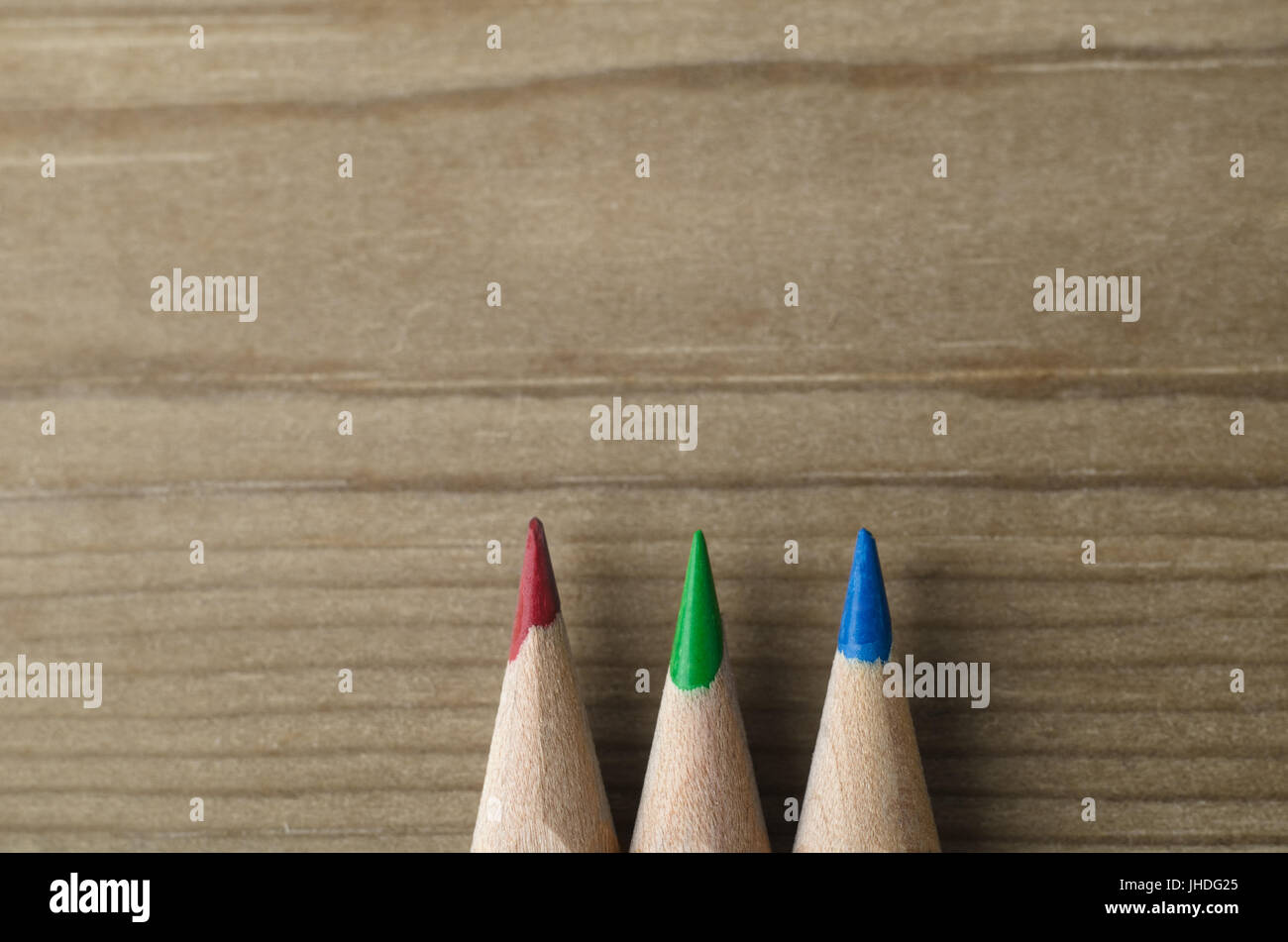 Three colour pencils pointing upwards into wooden background copy space. Represents the light-based RGB colour model. Stock Photo