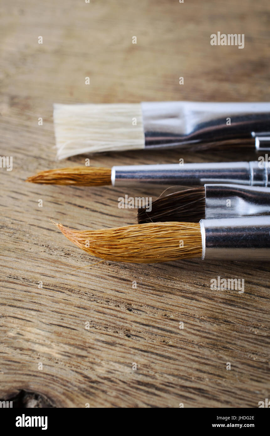 A row of clean, unused paintbrushes with a mixture of bristle types, lying on an oak wood table. Close up shot, just above eye level. Stock Photo