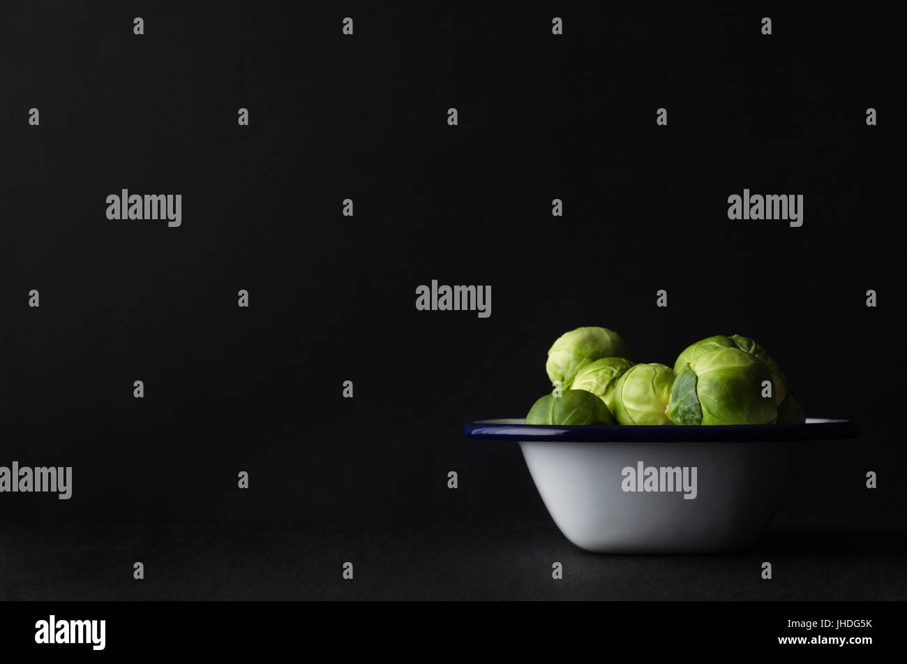 Brussel Sprouts, piled up high in a white and blue enamel baking tin on black surface.  Chalkboard background provides copy space to left and above. Stock Photo