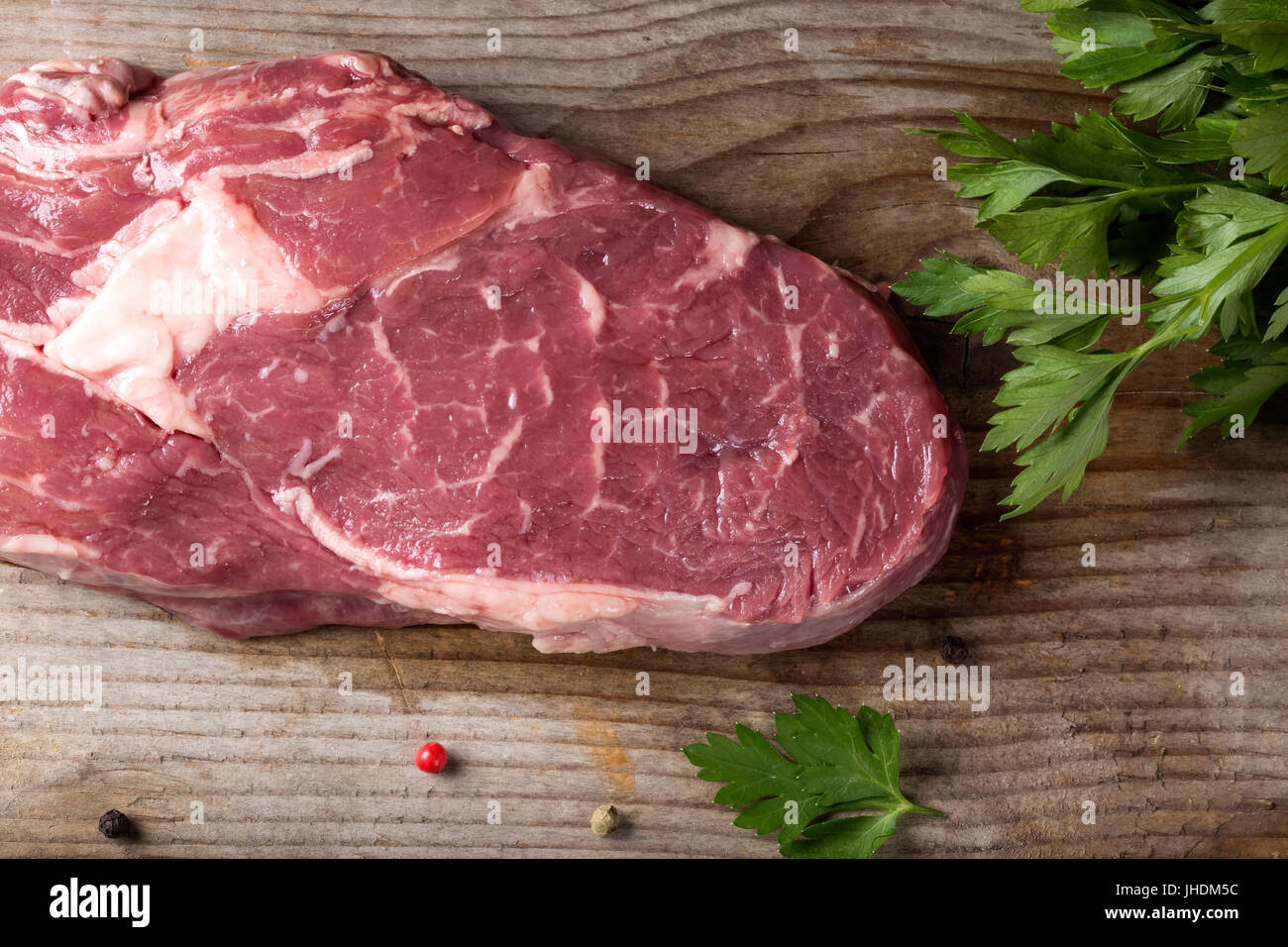 Raw Rib Eye Steak with parsley on wooden rustic background - top view Stock Photo