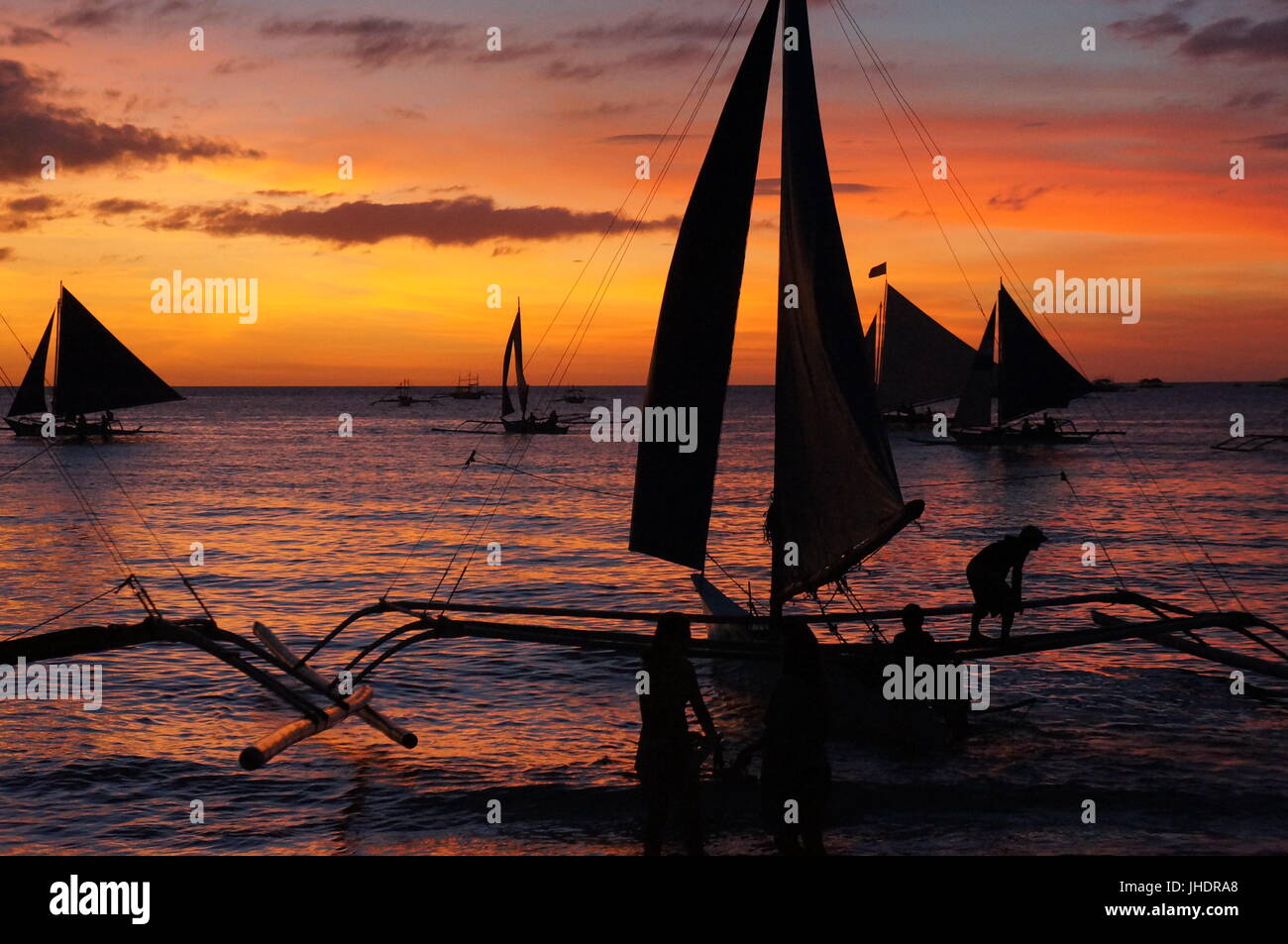 Stunning tourist board style photo. beach sunset view silhouette of sailing boats background, with man standing on outriggers.  Boracay Philippines . Stock Photo