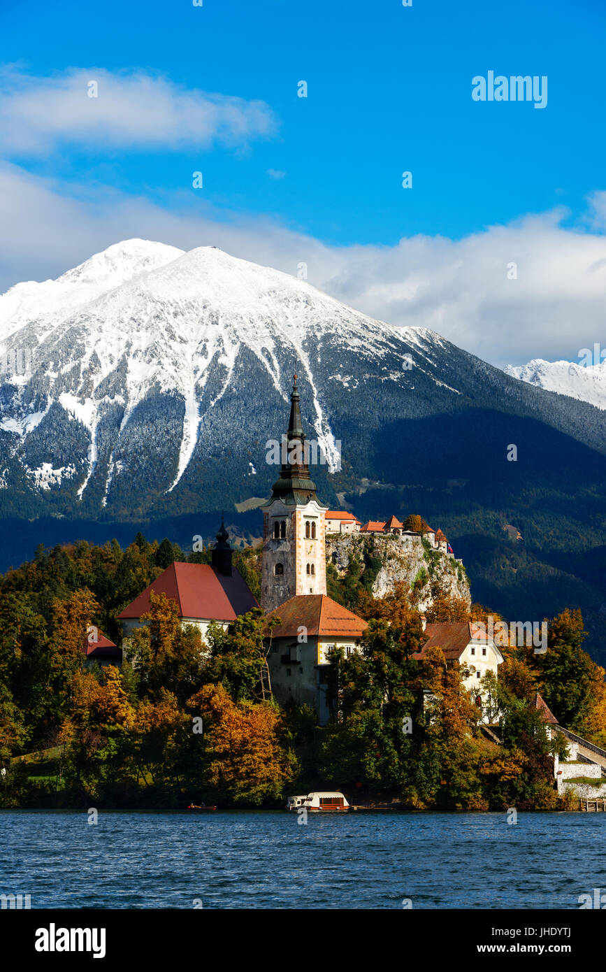 The church on the island in Lake Bled with in the background Bled castle and snow-capped mountains with trees in fall colors during autumn in Bled, Sl Stock Photo