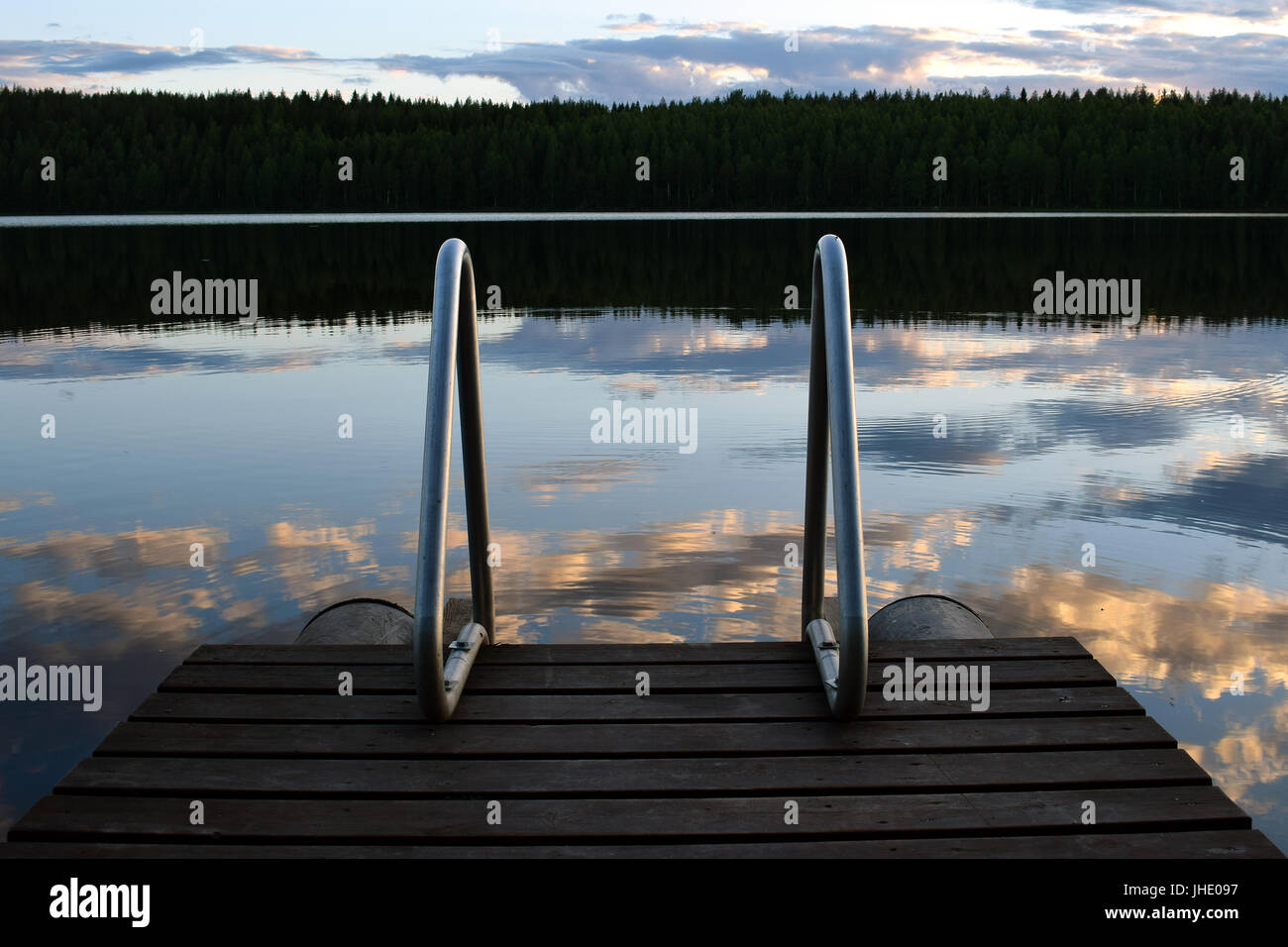 Ladder into lake from wooden swimming pier on summer night in central Finland. Stock Photo