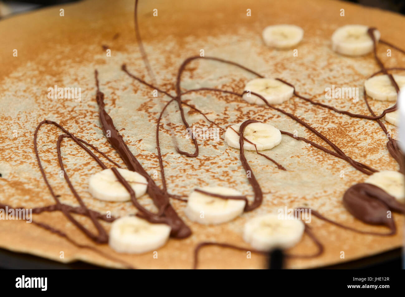 drizzling chocolate nutella onto crepe with bananas Stock Photo Alamy
