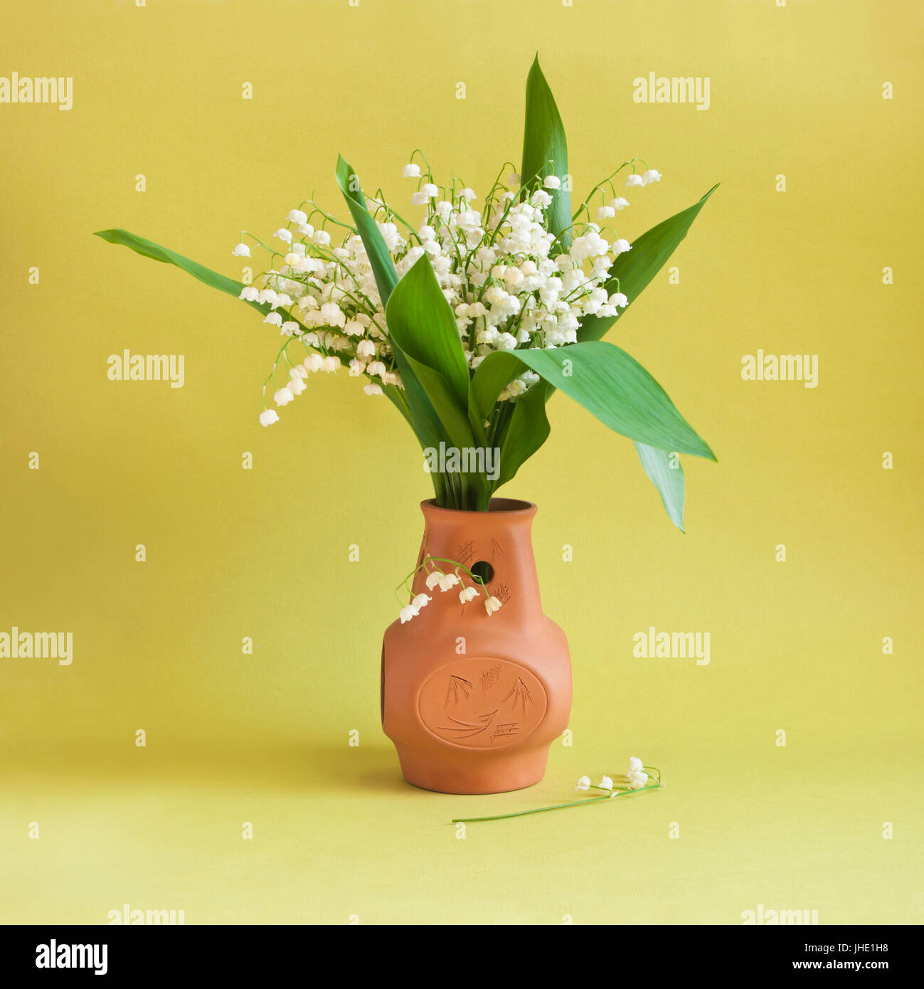 lily-of-the-valley in clay vase on yellow background Stock Photo