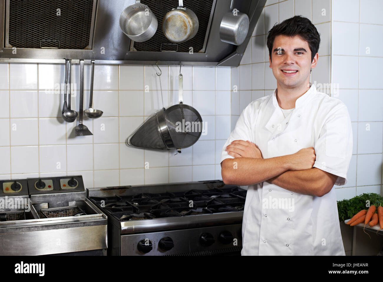 Portrait Of Chef Wearing Whites Standing By Cooker In Kitchen Stock