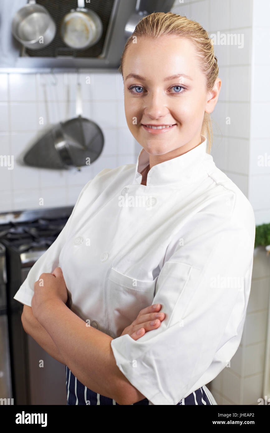 Portrait Of Female Chef Wearing Whites Standing By Cooker In Kitchen Stock Photo