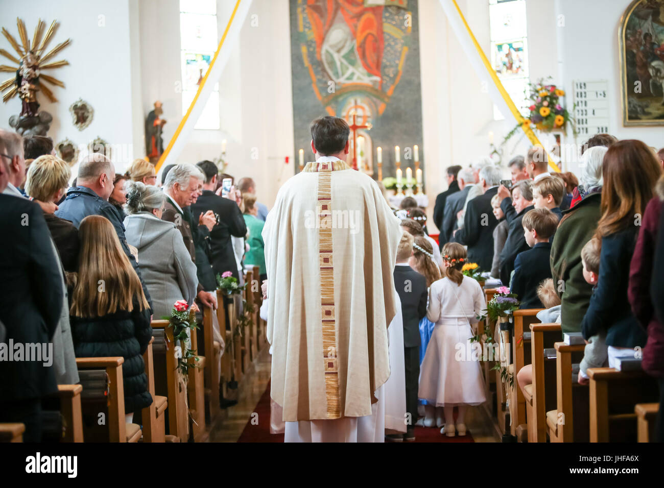 NANDLSTADT, GERMANY - MAY 7, 2017 : A rear view of the priest standing in the church isle with a group of young communicants between pews full of peop Stock Photo