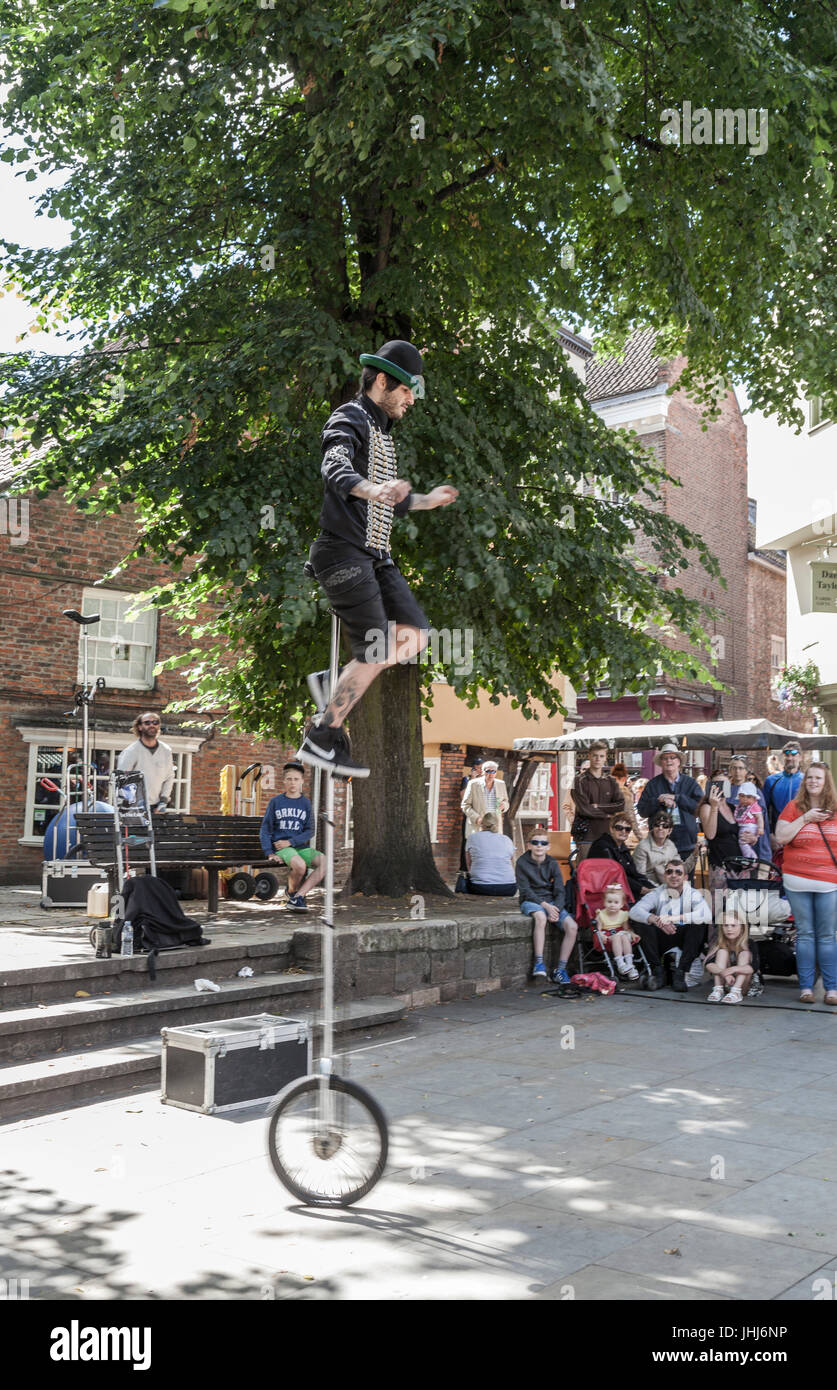 A hooded street entertainer on a unicycle and juggling burning torches